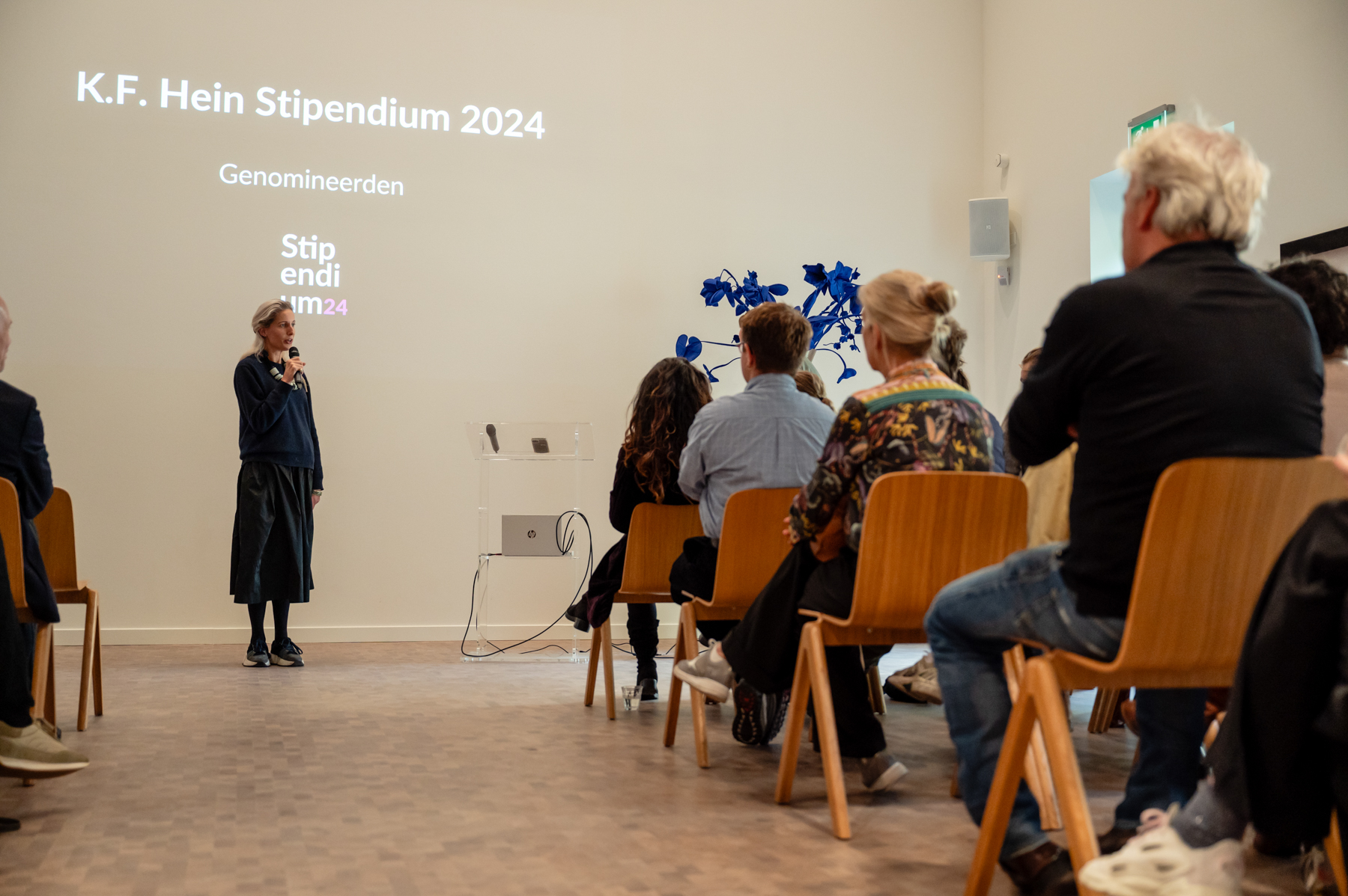 directeur Anna Kesler van het K.F. Hein Fonds staat voor de zaal en vertelt over het stipendium